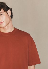 Bawełniany t-shirt w kolorze rdzy, z okrągłym dekoltem i krótkimi rękawami, o gładkiej fakturze i prostym wzornictwie.