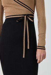 Brązowy sweter z dzianiny w czarne paski, zestawiony z czarną spódnicą o prążkowanej strukturze, z brązowym paskiem w talii. Teksturowana tkanina, dopasowany krój, długość do połowy uda.