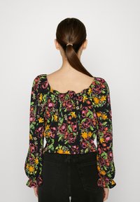 Floral top van zwarte stof met kleurrijke rozen en gele bloemen. Lange puffmouwen met elastische manchetten en een vierkante halslijn.