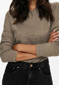 Grauer Strickpullover mit Rundhalsausschnitt und gerippten Bündchen, kombiniert mit hochtaillierten schwarzen Jeans aus Denim mit kupferfarbener Hardware.