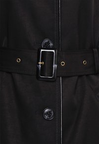 Czarny płaszcz z wyraźnym paskiem z prostokątną srebrną klamrą, czarnymi guzikami i gładką teksturą materiału.