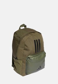 Sac à dos en nylon vert avec une forme arrondie, featuring des rayures noires, une poche avant et une section inférieure texturée.