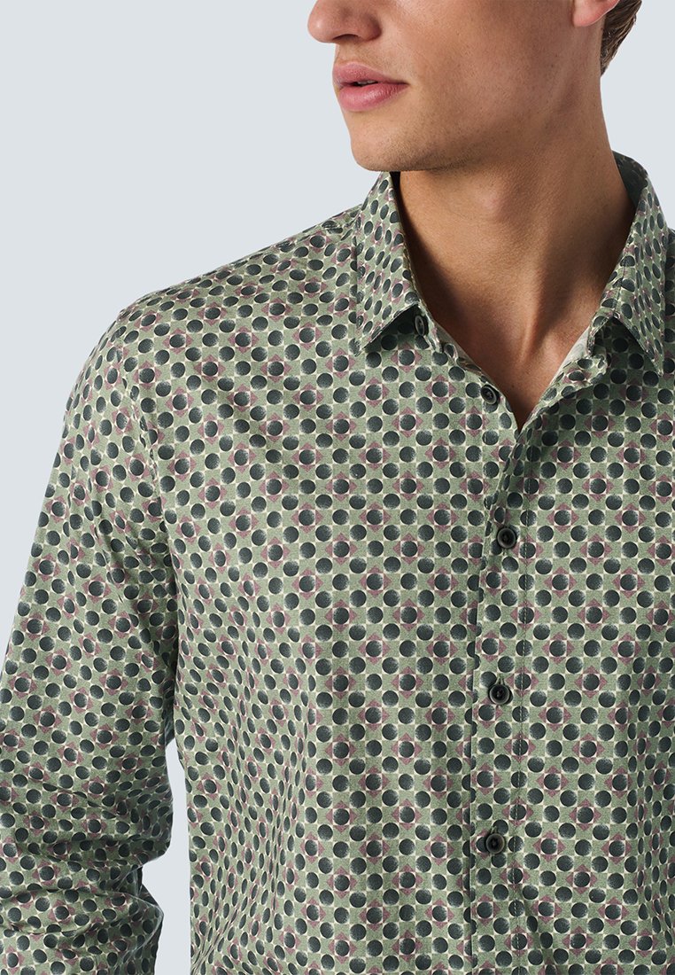 Grün gemusterte Hemd mit einem wiederkehrenden Kreisdesign in dunklerem Grün und Burgunderrot, mit einem klassischen Kragen und Knopfverschluss.