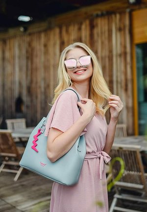 Světle modrý hobo batoh s růžovým zigzag přívěskem, vyrobený z hladkého materiálu. Obsahuje nenápadné logo značky a odolné uchopovací popruhy.