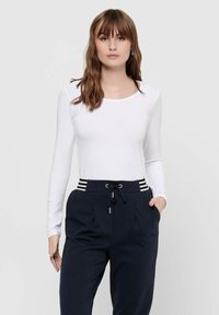 Langärmliges weißes Oberteil mit Rundhalsausschnitt, kombiniert mit navyblauen Hosen, die gestreifte Akzente am Bund und eine Kordelzugverschluss haben.