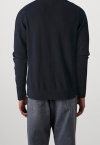 Granatowy sweter dzianinowy z długimi rękawami i dekoltem w kształcie V, w połączeniu z szarymi dżinsami o klasycznym designie pięciu kieszeni.