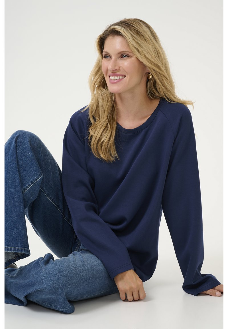 Un haut à manches longues bleu marine avec un col rond, coupe décontractée et texture douce. Associé à un jean flare bleu clair.