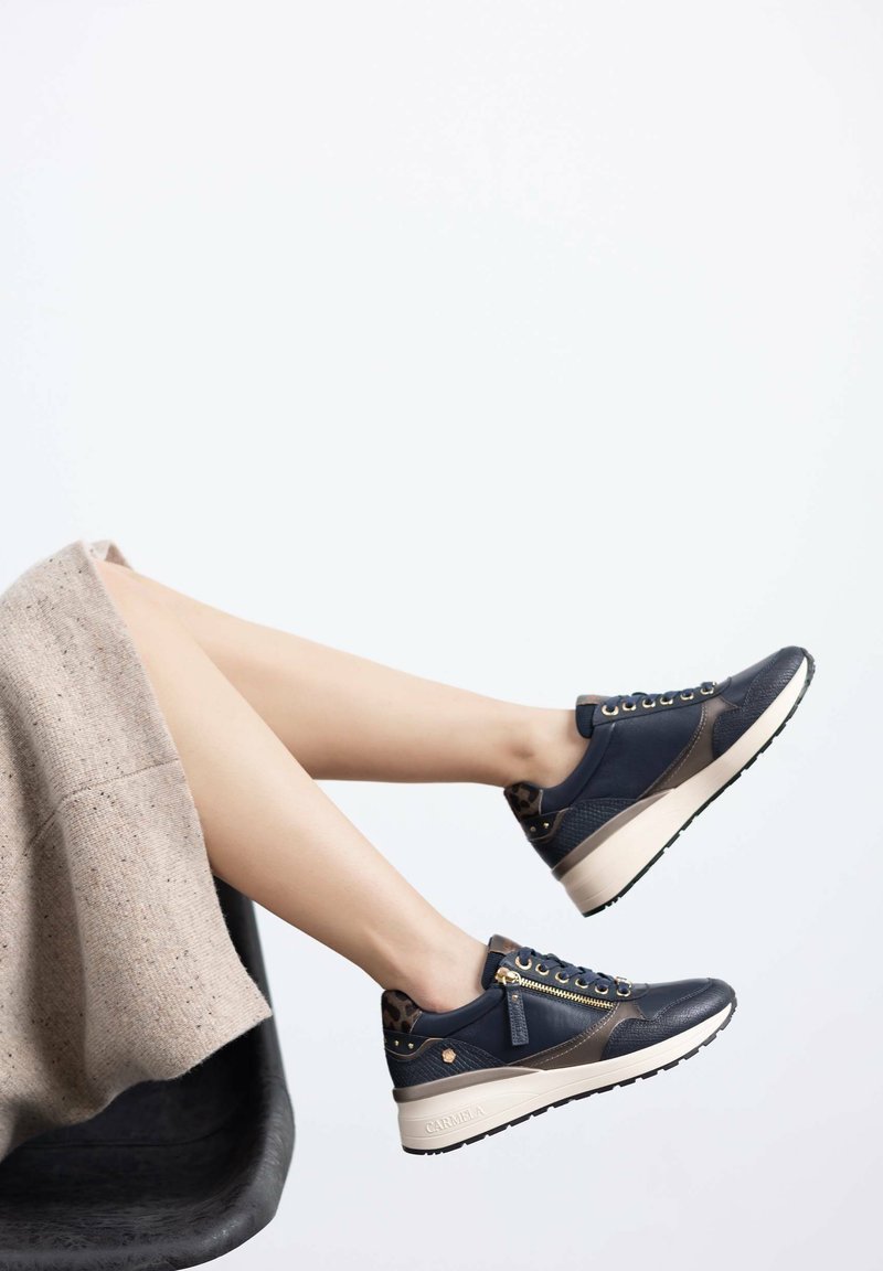 Zapatillas deportivas azul marino con un acabado texturizado, ojales dorados y una suela de plataforma bicolor. Detalladas con acentos de estampado de leopardo.