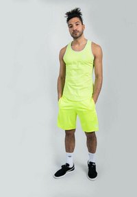Canotta senza maniche di un giallo neon e pantaloni corti abbinati, realizzati in un tessuto liscio. Presenta un collo rotondo e tasche laterali. Sneakers nere completano l'outfit.