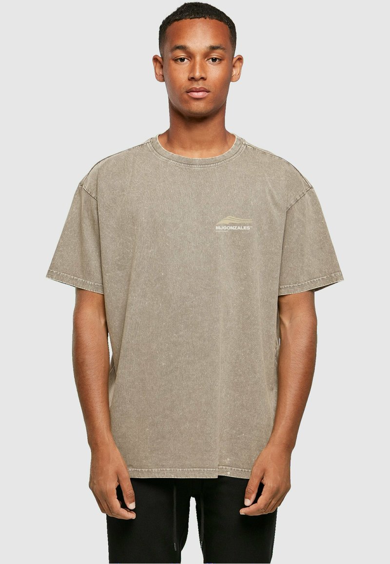 Tricou gri oversized cu mânecă scurtă din material bumbac, cu guler rotund și un mic logo pe partea stângă a pieptului. Textură moale.