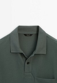 Polo à manches courtes vert foncé avec col, patte de boutonnage à deux boutons et poche poitrine, posé à plat sur un fond blanc.