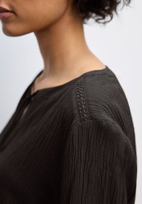 Top in tessuto nero con texture, dal collo arrotondato, caratterizzato da dettagli di cucitura sottili sulle cuciture delle spalle e una vestibilità comoda.
