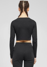 Crni dugi rukav uski crop top od glatkog materijala, s okruglim izrezom i prilagođenom siluetom. Uparite s crnim hlačama visokog struka.