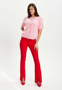 Light pink short-sleeve sweater with buttons and floral accents, paired with fitted red pants featuring split hems and matching red high heels.