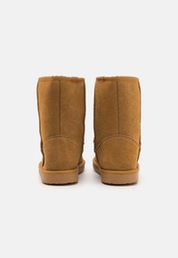 Bruna mocka ankelskor med en slät yta, rundade toppar och en lätt gummisula, med dubbla sömmar och minimal dekoration.