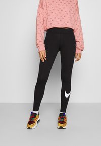 Svarta leggings med en vit Nike-logga, matched med en rosa kortärmad sweatshirt med ett upprepande mönster. Färgglada flerfärgade sportskor med snören.