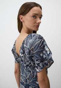 Marineblauw bloemenjurk met korte pofmouwen, een diepe V-rug en een gladde stof met bladeren- en bloemenpatronen in wit en perzik.