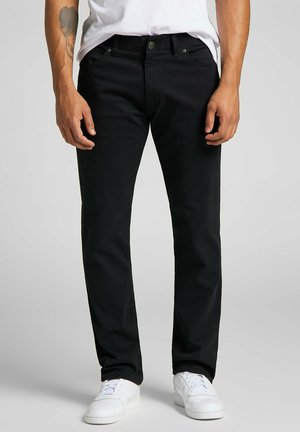 Jeans de mezcla de algodón negros con corte recto, diseño de cinco bolsillos, presillas para cinturón y un acabado sutil. Combinados con zapatillas blancas.