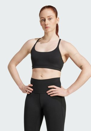 Svart sportsbh med tynne stropper, med en scooped halsringning. Kombinert med høyhalset svarte leggings, glatt tekstur, minimale detaljer.