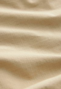 Țesătură bej cu un model fin, texturat. Suprafața apare netedă, cu o strălucire subtilă și o cădere blândă, evidențiind calitatea sa ușoară.