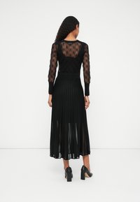 Un vestido negro con un top transparente y texturizado y una falda plisada semi-transparente. Estilizado con tacones altos negros.