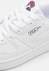 Sneaker bianca in pelle sintetica con accenti in rete. Presenta lacci bianchi spessi, una patch con logo sulla linguetta e cuciture a contrasto.