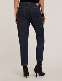 Jeans de mezclilla azul oscuro con una cintura de altura media, patas ajustadas y dos bolsillos traseros. Presenta una etiqueta de logo marrón en la cinturilla y costuras en contraste.