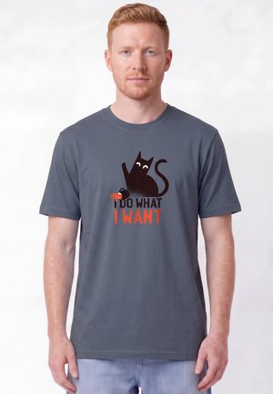 Homme portant un t-shirt gris avec un motif de chat noir et le texte "I do what I want", tenant un petit crabe rouge sur fond blanc.