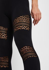 Svarta leggings med genomskinliga spetsinsatser med ett blommönster vid låren. Mjuk tygkvalitet med en figurnära design och texturerad detalj.