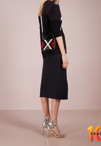 Felpa nera con dettagli bianchi, gonna midi nera, décolleté a stiletto argento metallizzato con dettagli a stella, e una piccola borsa a tracolla multicolore.