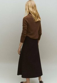 Un pull marron à côtes associé à une longue jupe noire. La tenue présente un design simple et une texture douce, convenant pour un port décontracté.