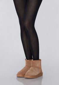 Bottines en suède beige à bout arrondi, avec des bordures côtelées et une semelle en caoutchouc, portées avec des leggings transparents noirs.