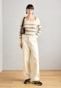 Striped ribbed sweater in yellow and brown, paired with beige wide-leg pants and black sneakers, complemented by a brown shoulder bag.