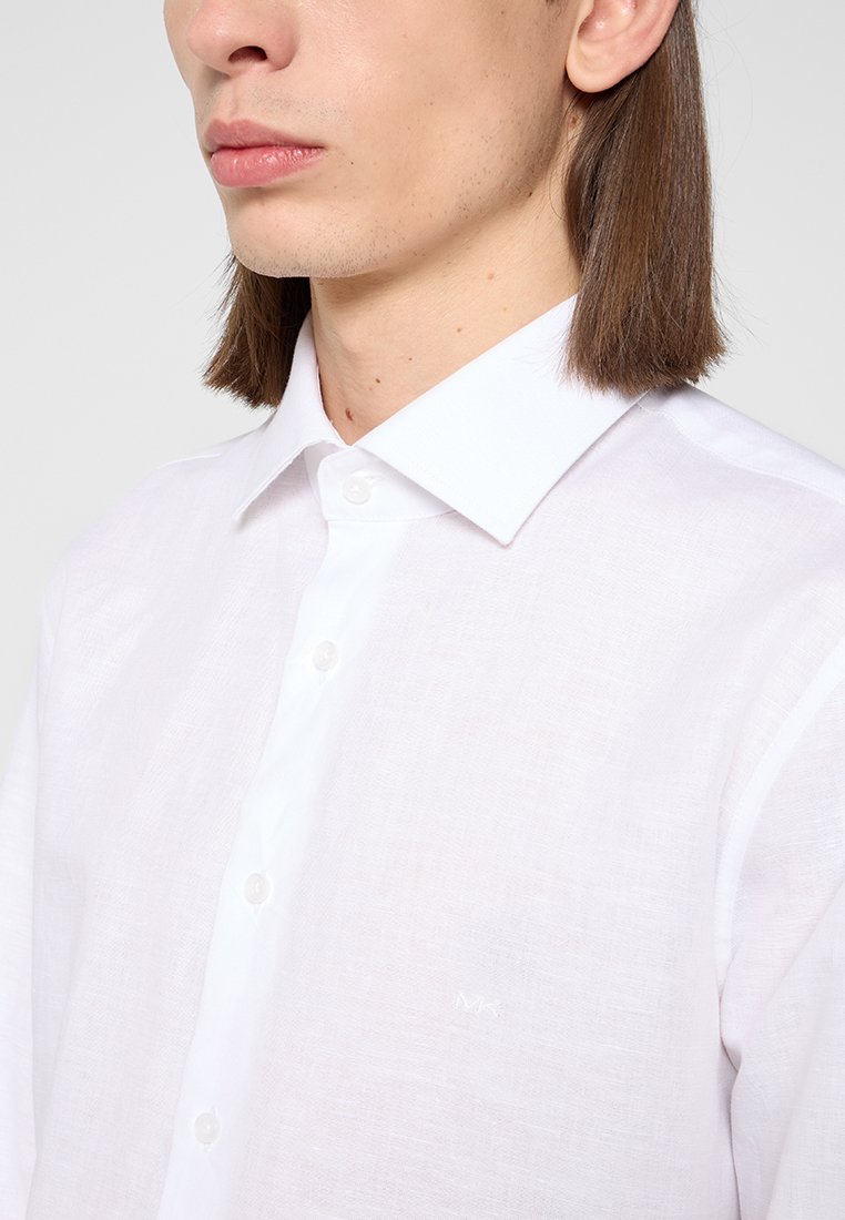Biała lniana koszula z guzikami i klasycznym kołnierzykiem. Posiada subtelną teksturę oraz pięć guzików, z małym logo wyhaftowanym na piersi.
