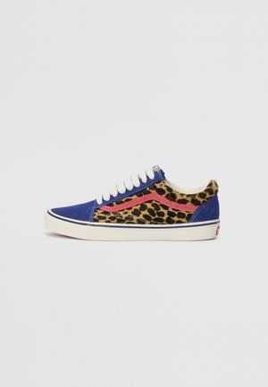 Niedriger Sneaker mit blauer Wildlederkappe und Ferse, Leopardenmuster an den Seiten, rotem Streifen, weißen Schnürsenkeln und weißer Sohle mit schwarzem Rand auf grauem Hintergrund.