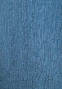 Tissu bleu texturé avec des plis verticaux, lisse au toucher, doté d'un léger éclat et de coutures visibles le long de l'ourlet.