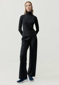 Top negro de manga larga con cuello alto y diseño ceñido, combinado con pantalones negros de pierna ancha. Zapatillas texturizadas completan el conjunto.