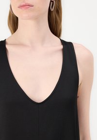 Svart ärmlös topp med djup V-urringning, tillverkad av slätt tyg; har rena linjer och en minimalistisk design.