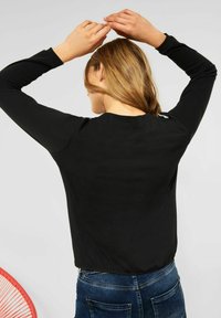Svart långärmad topp med rund halsringning, mjukt tyg och slät textur. Har en figurnära silhuett och diskret axeldetaljering.