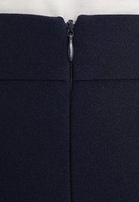 Tissu bleu marine au toucher lisse avec une fermeture éclair centrale et des finitions de couture soignées. Le tirant de la fermeture éclair est en gris métallique.