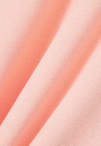 Tela suave y ligera en un tono coral claro, con una textura de punto fina y sutiles variaciones en la intensidad del color.