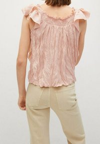 Vaaleanpunainen hihaton toppi, jossa on röyhelöillä varustetut olkaimet, smockattu kaula-aukko ja teksturoitu kangas. Yhdistetty vaaleisiin, istuviin farkkuihin.