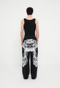 Μαύρο αμάνικο τοπ και φαρδιά παντ ελόνια φόρμας με μεγάλο λευκό γραφικό σχέδιο και σούρα στη μέση, με περίτεχνα μοτίβα στην πλάτη.