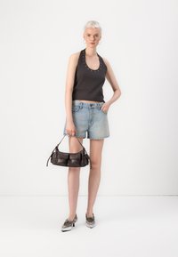 Débardeur gris foncé avec des détails en œillets argentés, shorts en denim bleu clair et un petit sac à main marron foncé. Des chaussures argentées avec lacets complètent le look.