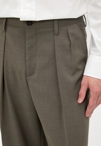 Fållade byxor i en dämpad olivgrön tyg, med knappstängning, sidofickor och en slät textur. Skräddarsydd design med en elegant finish.