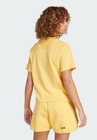 Conjunto deportivo amarillo que incluye una camiseta de manga corta y pantalones cortos. La tela es suave con un corte relajado, mostrando una mínima marca en el dobladillo.