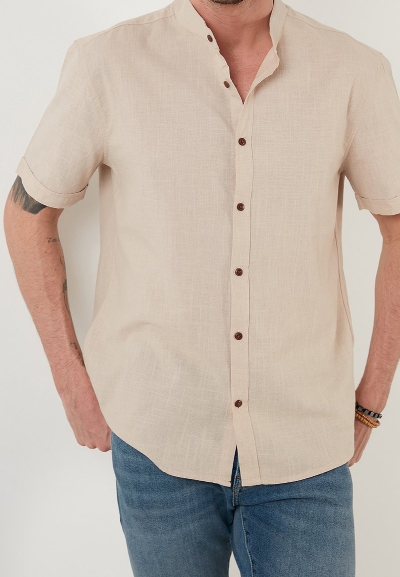 Beige overhemd met korte mouwen en een mandarinakraag, voorzien van bruine knopen. Gemaakt van textuurstof, heeft een rechte snit en een subtiel geweven patroon.