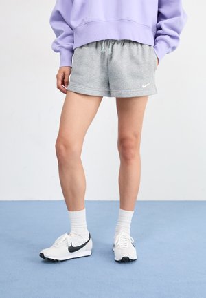Shorts en coton gris avec une taille élastique, associés à des chaussettes blanches et des chaussures Nike avec des accents noirs. Un sweat-shirt oversize lavande est porté.