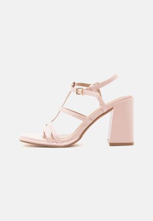 Sandale à talon haut rose avec talon bloc, bride à la cheville, fermeture à boucle et plusieurs fines lanières sur le pied.