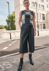 Plišani prsluk sa karo uzorkom u plavoj, smeđoj i bijeloj boji; crne bermude visokog struka od umjetne kože; crne gležnjače šiljatog vrha.